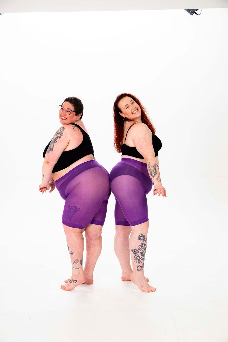 Anti chafing shorts collection: two women in purple anti chafing shorts and black bras posing back-to-back to showcase better tights